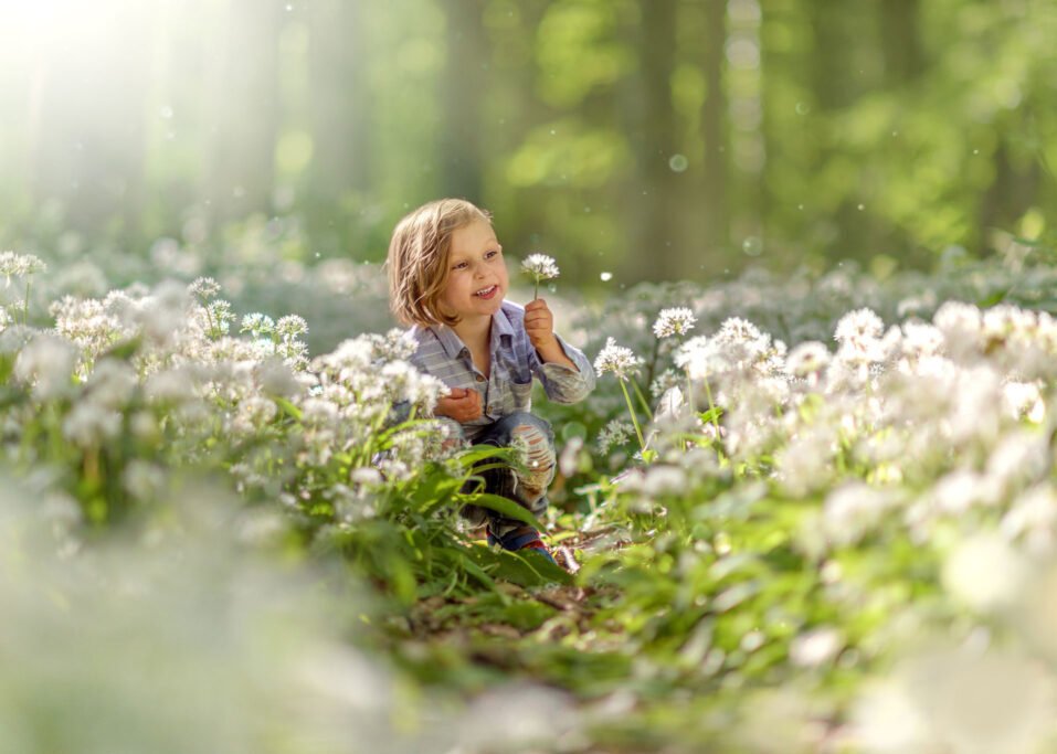 A joyful child sits in a sunlit field of wild garlic in Nottingham, a perfect moment captured during a family photoshoot.