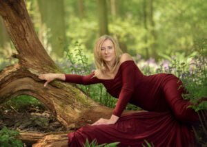 Woman in a deep blue dress standing elegantly among bluebells in Nottingham’s woodland during a spring photoshoot.