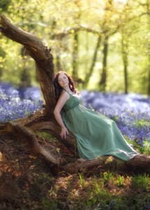 Woman in a green dress leaning on a fallen log surrounded by bluebells in Nottingham's enchanted woods.