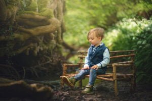 A thoughtful toddler takes a quiet moment to themselves on a rustic wooden bench in a Nottingham forest, embodying the spirit of a family photoshoot in nature.