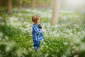 A child with headphones around their neck stands contemplative in a Nottingham wild garlic forest, a moment of connection with nature.