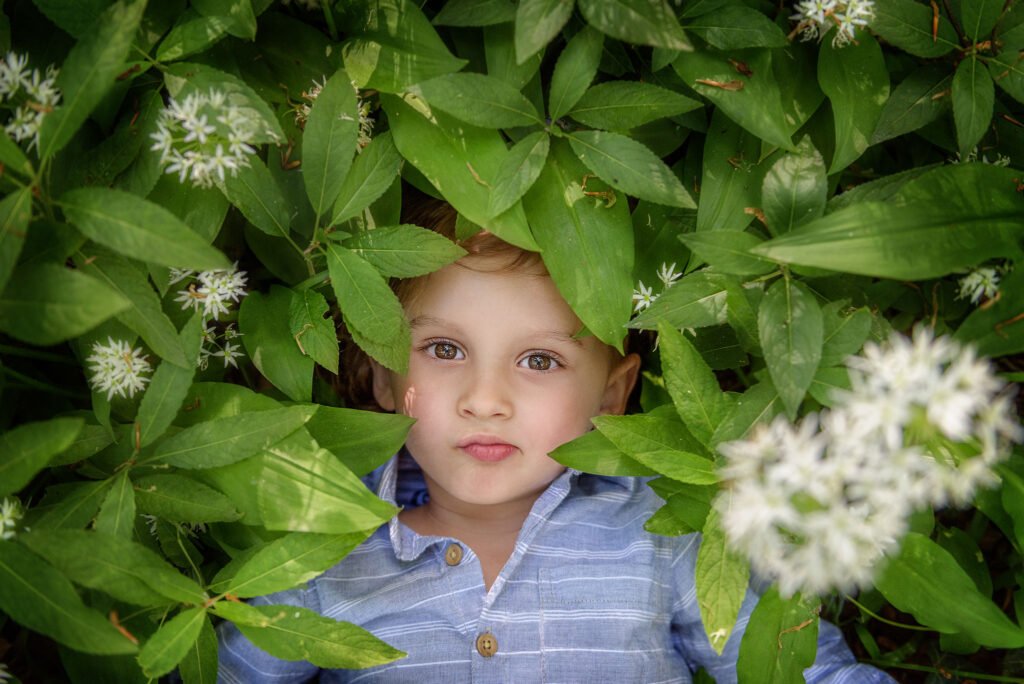 A serene child's face is framed by the verdant leaves and soft white blooms of wild garlic, embodying the peace of a Nottingham family photoshoot.