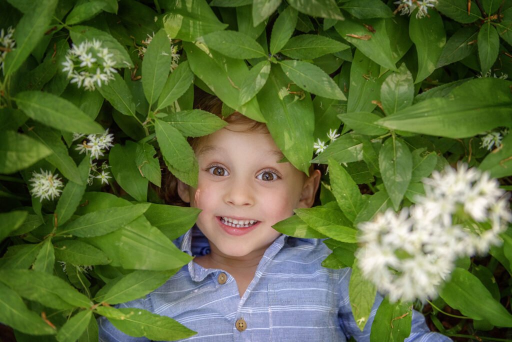 A child's beaming face emerges amidst a lush green sea of wild garlic flowers, capturing the joy of a family photoshoot in Nottingham.