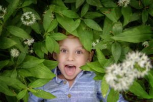 Excitement and wonder light up a child's face peeking through the lush leaves and blossoms of Nottingham's wild garlic.