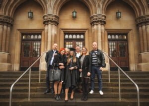 A graduate in academic regalia celebrating with family on the steps of a historic Nottingham university building.