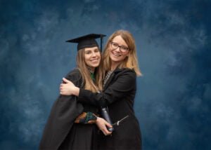 A graduate in academic regalia hugging her friend during a Nottingham graduation photoshoot.
