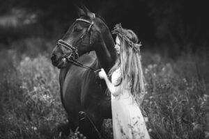Black and white photo of a woman with her horse in a floral field during an equine photoshoot"