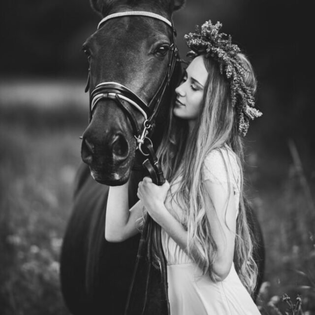Black and white photo of a woman standing closely with her horse during an equine photoshoot
