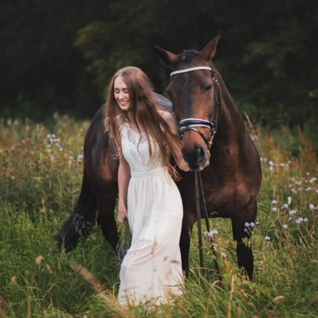 Young woman walking with her horse in a field during an equine photoshoot