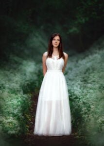 Woman in white lace dress for photoshoot standing in forest setting