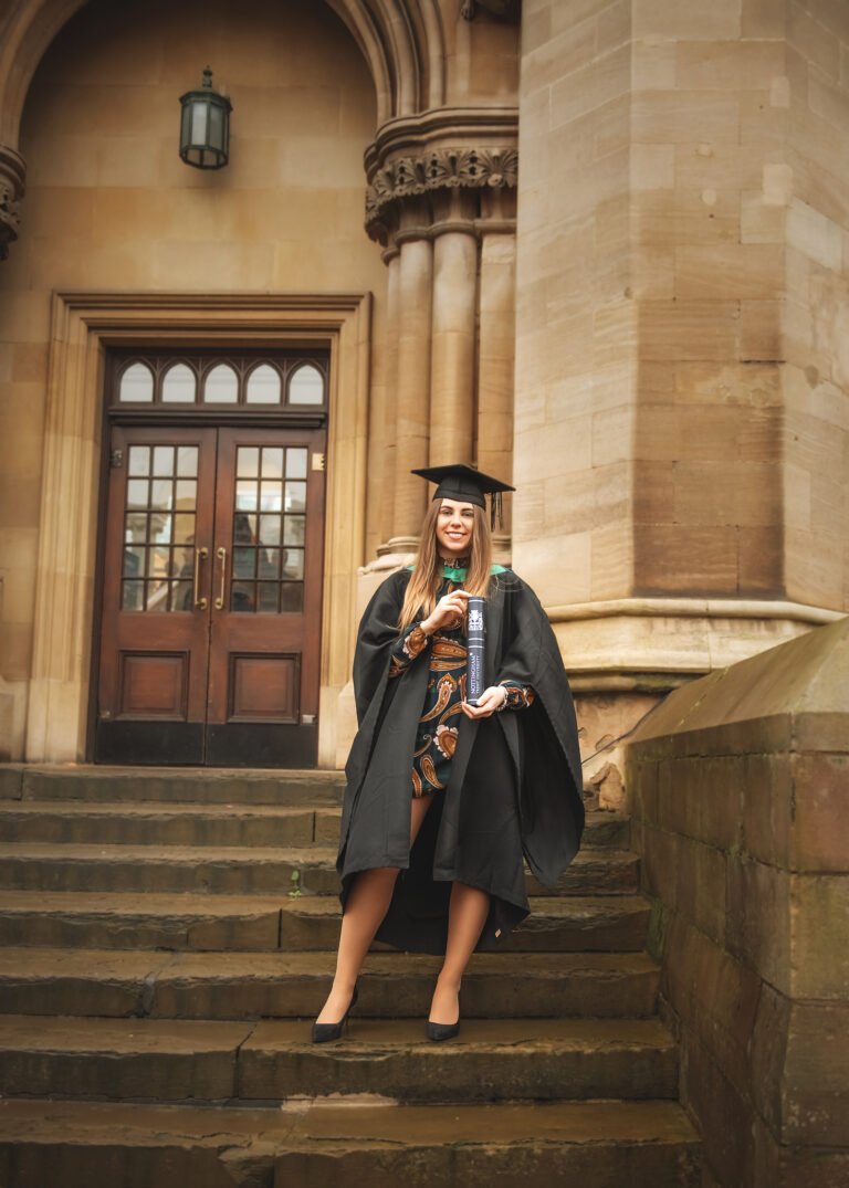 Smiling graduate with diploma in front of the historic architecture at Nottingham Trent University on graduation day