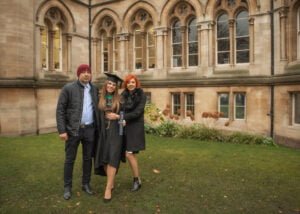 A graduate standing with her parents on the lush Nottingham University campus, holding a diploma.