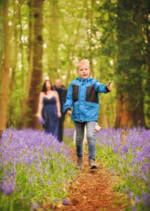 Young boy leading the way through bluebell woods with family in the background during a photoshoot in Nottingham.