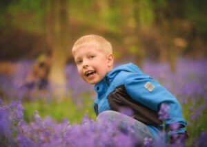 Smiling young boy surrounded by purple bluebells in a Nottingham woodland during a spring photoshoot.