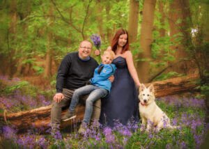 Family of three posing on a log surrounded by bluebells in Nottingham’s ancient woodlands during a family photoshoot.