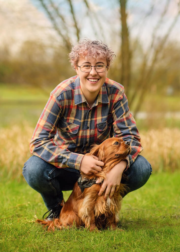 A cheerful individual with a bright smile shares a heartwarming embrace with a russet-colored spaniel in a vibrant, sunlit field.