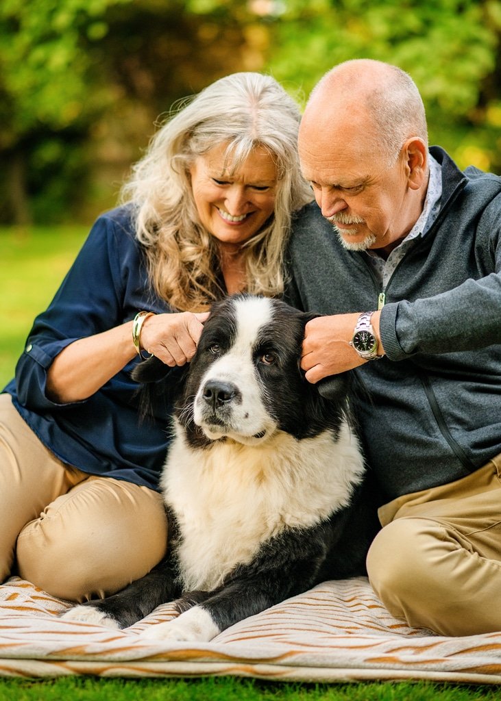 Joyful senior couple sharing a tender moment with their beloved Border Collie in a lush Nottingham garden, embodying the warmth of family and the expertise of a Nottingham dog photographer.