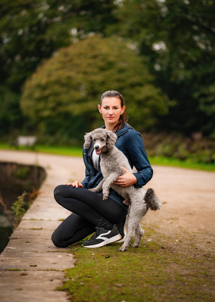 A woman shares a peaceful moment with her grey poodle on a tranquil path in Nottingham, reflecting the special bond in their companion animal portrait.