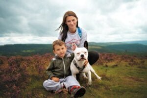 A mother and child share a serene moment with their white dog amidst the heather-covered hills, showcasing the natural beauty around Nottingham captured by a skilled dog photographer.