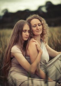 Mother and daughter embracing in a serene outdoor setting with matching neutral-toned dresses
