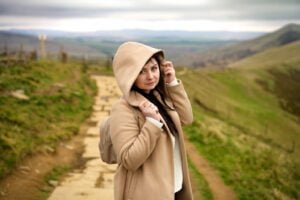 Marta Szulc, a contemplative family photographer, stands amidst a rolling landscape, embodying the serene beauty of outdoor maternity photography.