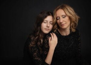 Mother and daughter in black lace dresses with eyes closed in an emotional studio photoshoot
