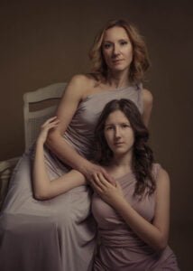 Mother and teenage daughter in soft-toned dresses, posing in a classic indoor portrait.