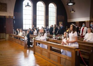 Children kneeling in church pews holding candles during a First Holy Communion ceremony.