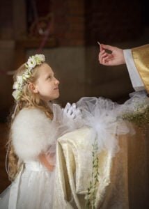 Young girl in a white dress receiving the Holy Eucharist during her First Holy Communion.