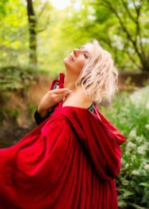 A woman draped in a vibrant red cloak looks upward with an air of serenity at her outdoor birthday photoshoot.
