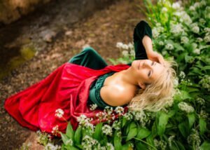 Woman in green dress and red cape lying among wildflowers, professional portrait.