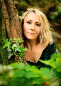 A woman peering through verdant foliage during her outdoor birthday photoshoot, embodying the spirit of the forest."