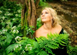 Thoughtful woman in green dress leaning against a tree looking upwards, professional portrait.