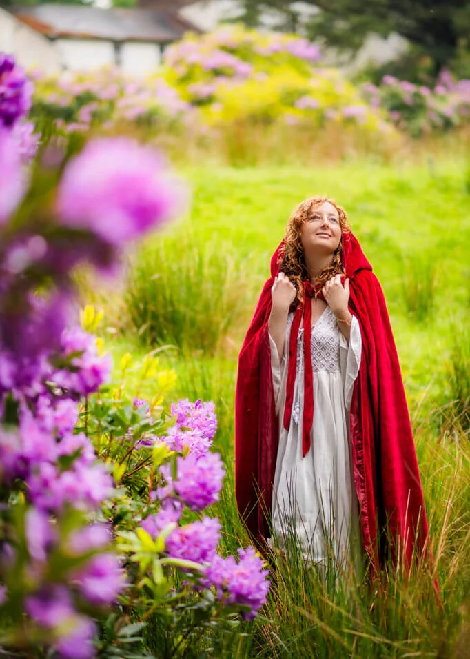 Woman in red cape among purple flowers in a professional women portrait.