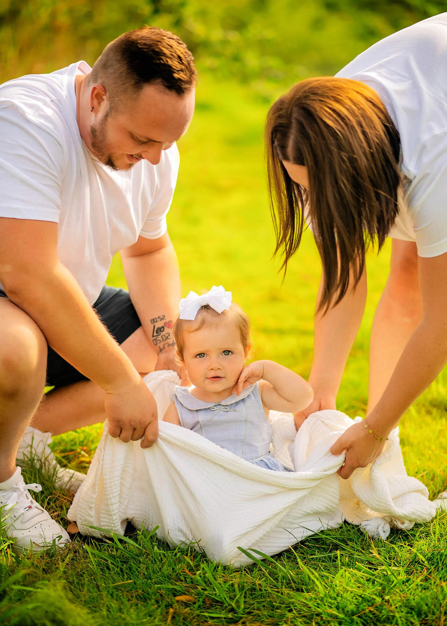 Parents with their baby on a grassy field during a relaxed family photoshoot for kids.