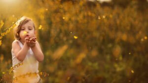 Child blowing flowers in a golden field during a photoshoot for kids in Nottingham.