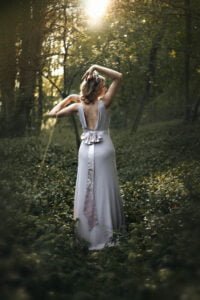 Professional portrait of a woman in silver dress in sunlit woods.