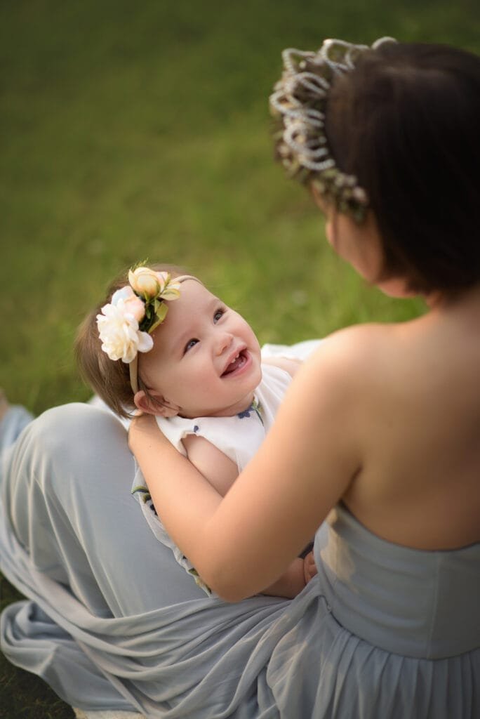 A joyful baby smiling while looking at her mother, captured in a tender moment of bonding in a natural outdoor setting.