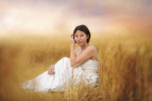A woman sits contemplatively in a golden field, the soft blur of nature harmonizing with her peaceful repose, reflective of breastfeeding photography's serenity.