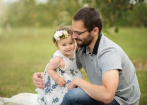 Father and daughter share a joyful moment outdoors, her smile as bright as the floral crown she wears.
