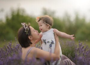 Mother holding her smiling baby in a lavender field, surrounded by soft purple blooms and greenery, celebrating motherhood and connection.