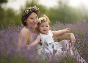 Smiling mother and baby in a lavender field, celebrating their bond with floral crowns and natural surroundings.