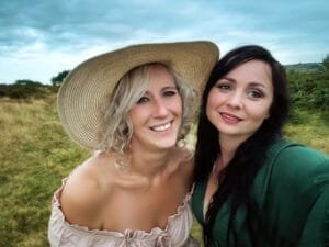 Two women smiling in a field, one wearing a straw hat, during a Nottingham friendship photoshoot