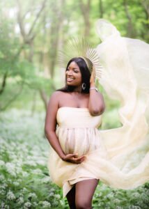A glowing expectant mother in a whimsical setting, her joy as luminous as the sunlit fabric swirling around her in a Nottingham forest.