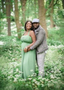 Expectant couple sharing a joyful embrace during their outdoor maternity photoshoot in a blooming forest.