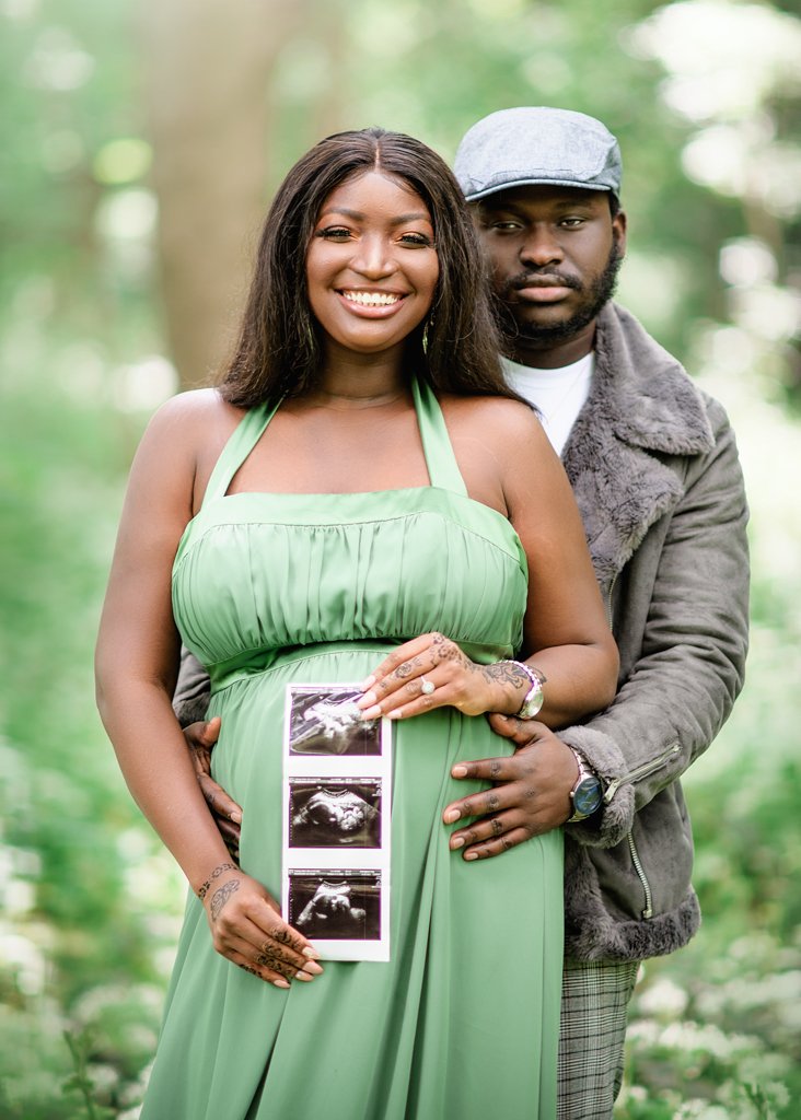 An expectant couple stands amidst a lush green backdrop, holding the first images of their unborn child, anticipation and love in their eyes.
