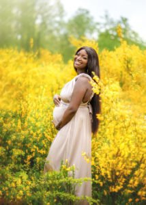 A radiant mother-to-be stands amidst a vibrant field of yellow flowers, her joy as bright as the blossoms around her.