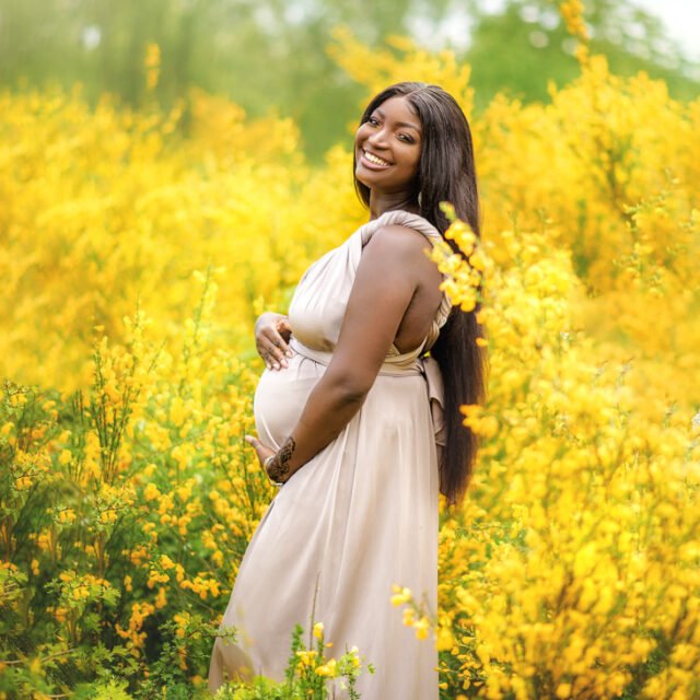 A radiant mother-to-be stands amidst a vibrant field of yellow flowers, her joy as bright as the blossoms around her.