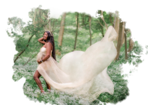 Expectant mother in a flowing cream gown cradling her baby bump during an outdoor maternity photoshoot in a lush green forest.