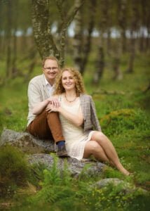Anniversary photoshoot in Nottingham forest with a couple seated on rocks surrounded by lush greenery